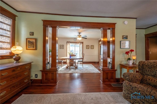 interior space with ceiling fan, dark wood-type flooring, ornamental molding, and ornate columns