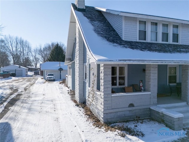 snow covered property featuring an outbuilding, covered porch, and a garage