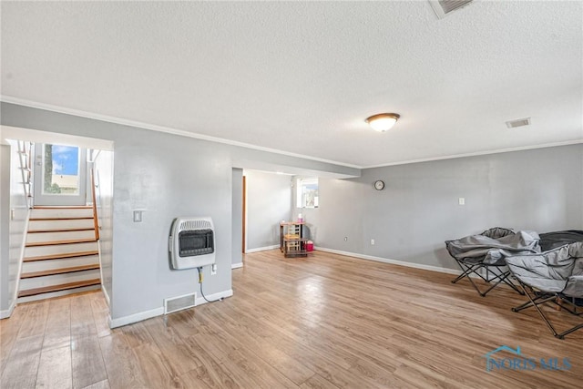 basement featuring light wood-type flooring, ornamental molding, a wealth of natural light, and heating unit