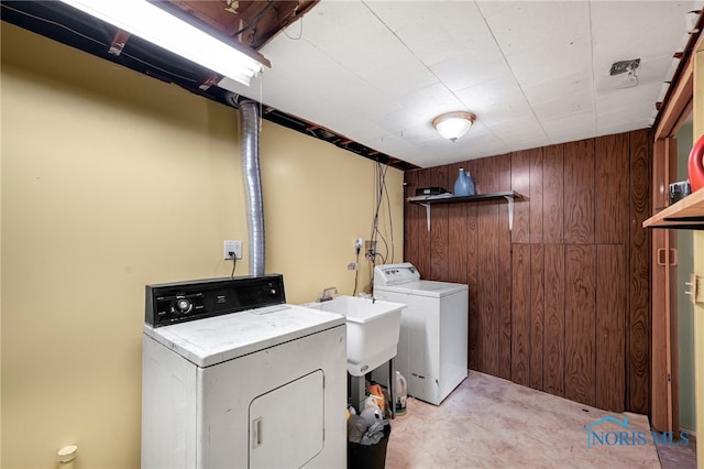 clothes washing area with wooden walls, sink, and washer and dryer