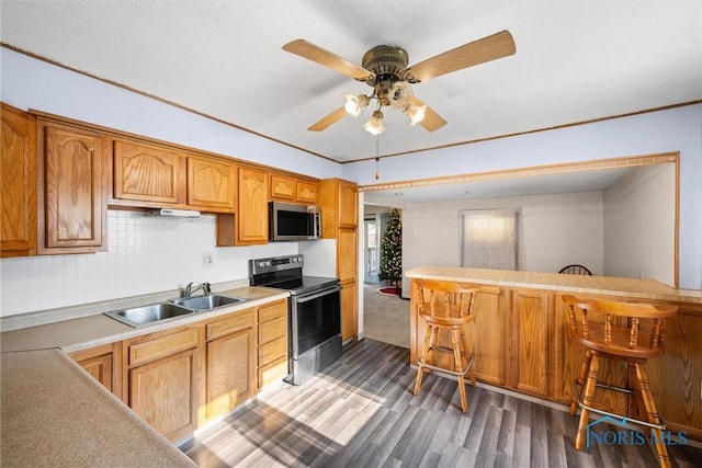 kitchen with kitchen peninsula, sink, dark wood-type flooring, a breakfast bar, and stainless steel appliances