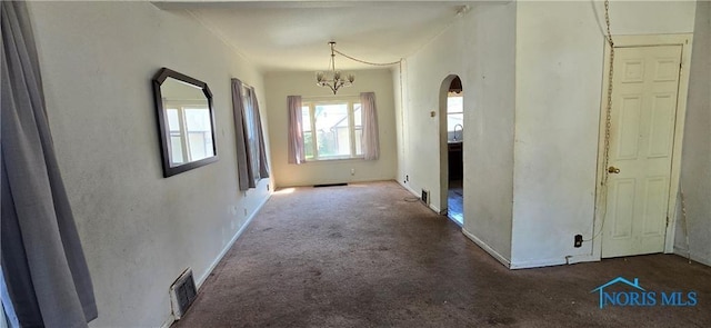 hallway with dark colored carpet and a notable chandelier