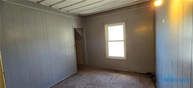 unfurnished room featuring light carpet and wooden walls