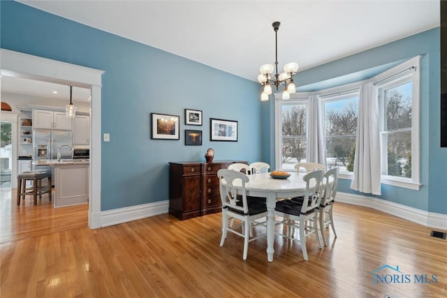 dining space with sink, light hardwood / wood-style flooring, and an inviting chandelier