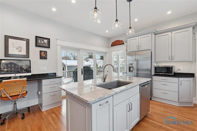 kitchen featuring appliances with stainless steel finishes, sink, pendant lighting, a center island with sink, and dark stone countertops