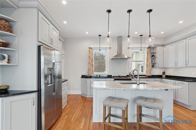 kitchen featuring pendant lighting, a kitchen breakfast bar, wall chimney exhaust hood, appliances with stainless steel finishes, and light hardwood / wood-style floors