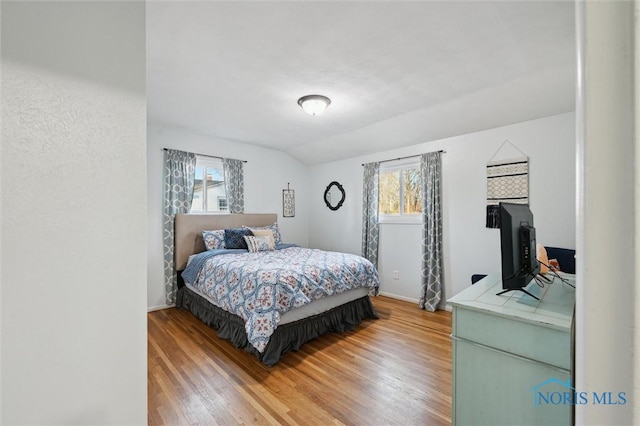 bedroom with wood-type flooring, vaulted ceiling, and multiple windows