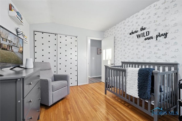 bedroom with hardwood / wood-style flooring, a crib, and vaulted ceiling