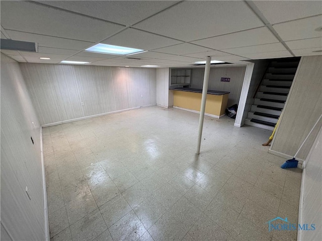 basement featuring a drop ceiling and wooden walls