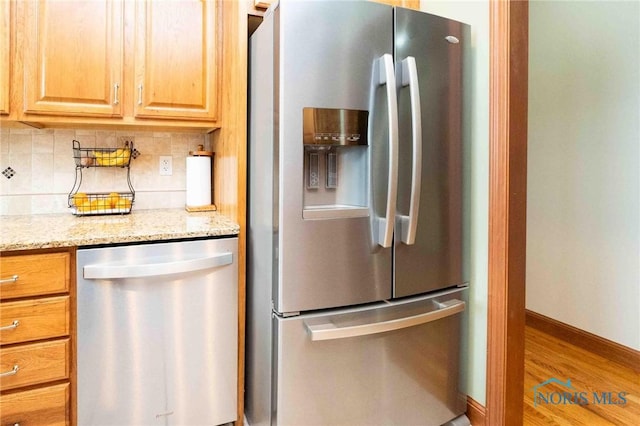 kitchen featuring hardwood / wood-style floors, decorative backsplash, light stone countertops, and stainless steel appliances