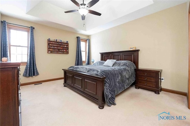 bedroom with a raised ceiling, ceiling fan, and light colored carpet