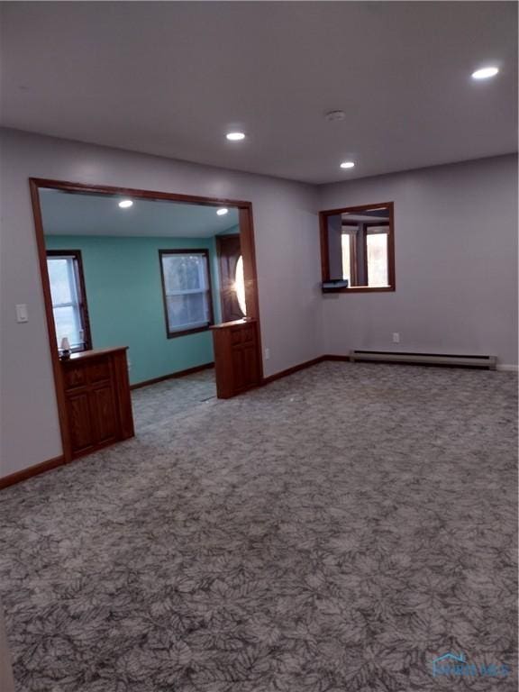 spare room featuring carpet, a healthy amount of sunlight, and a baseboard heating unit