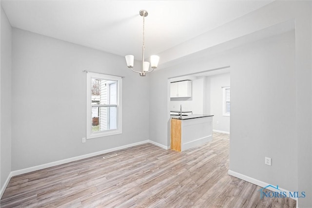 unfurnished dining area featuring a chandelier and light hardwood / wood-style flooring