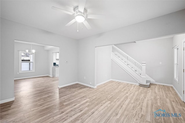 unfurnished living room with ceiling fan with notable chandelier and light hardwood / wood-style floors