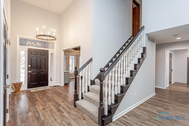 entryway with an inviting chandelier, a towering ceiling, and dark hardwood / wood-style flooring