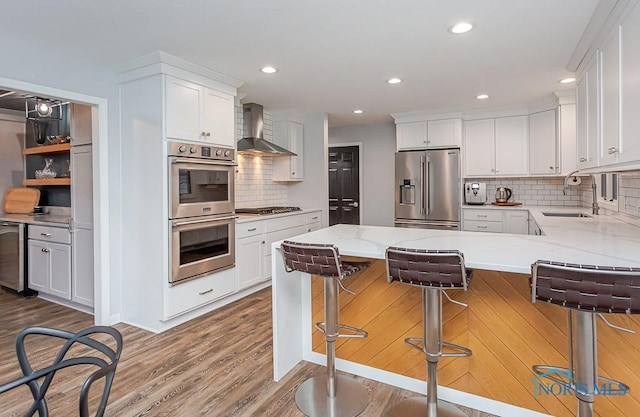 kitchen with wall chimney range hood, a breakfast bar area, white cabinetry, backsplash, and stainless steel appliances