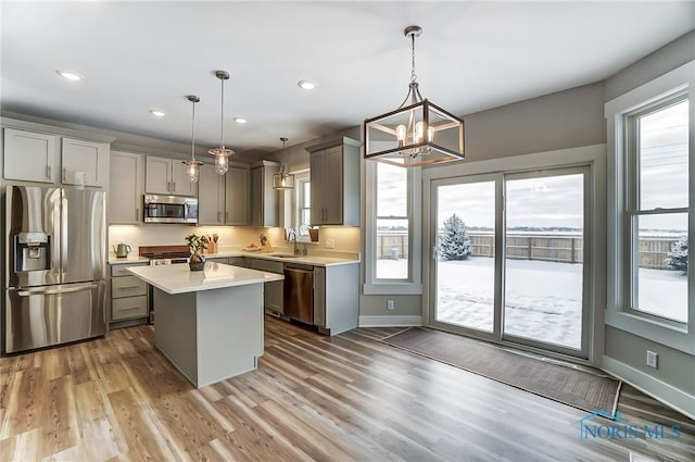 kitchen with hardwood / wood-style flooring, gray cabinets, appliances with stainless steel finishes, decorative light fixtures, and a kitchen island