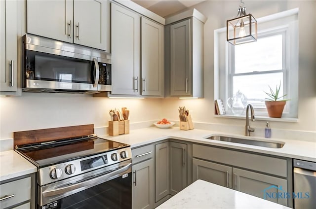 kitchen featuring appliances with stainless steel finishes, gray cabinets, pendant lighting, and sink