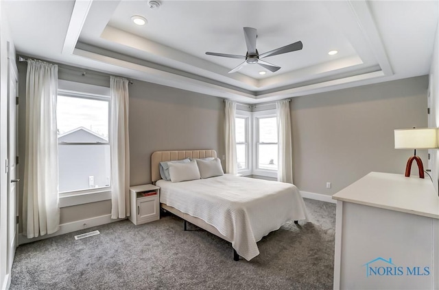 carpeted bedroom with a raised ceiling, multiple windows, and ceiling fan