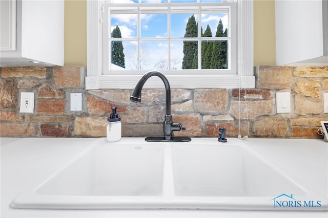 room details featuring backsplash, white cabinetry, and sink