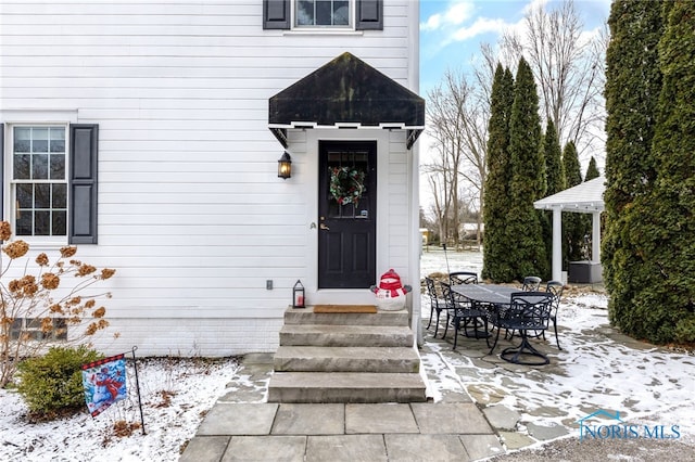 snow covered property entrance with a patio