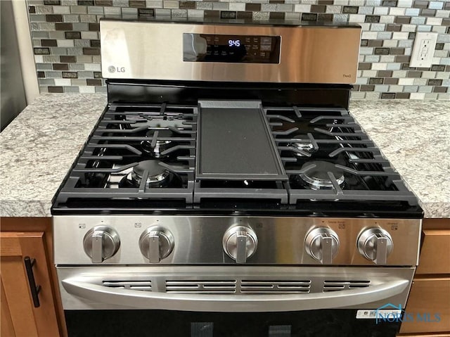 interior details featuring decorative backsplash, light stone countertops, and stainless steel gas range