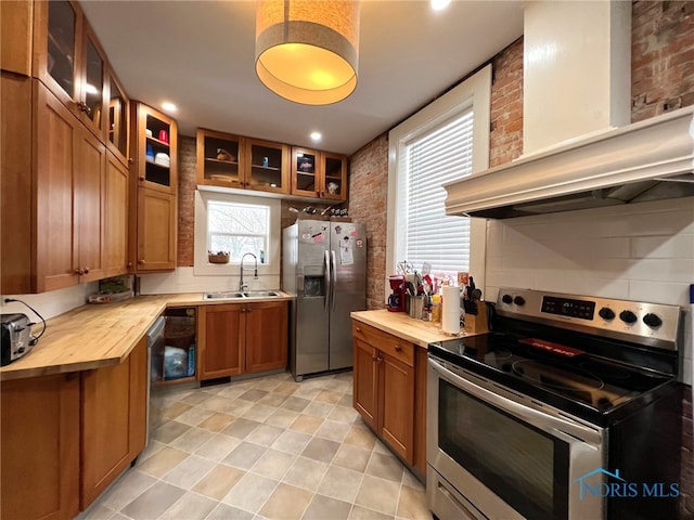 kitchen featuring wall chimney exhaust hood, butcher block counters, sink, tasteful backsplash, and stainless steel appliances