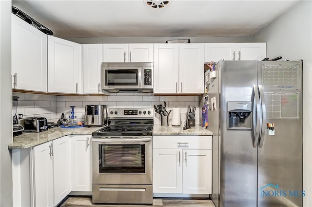 kitchen featuring backsplash, light stone countertops, white cabinets, and appliances with stainless steel finishes