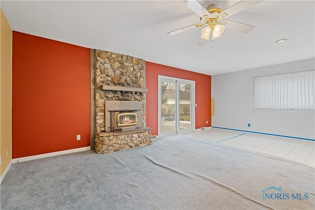 unfurnished living room with ceiling fan, a stone fireplace, and carpet