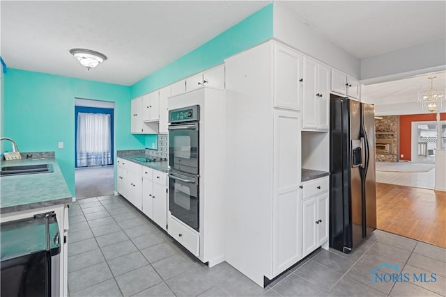 kitchen featuring sink, light tile patterned floors, black appliances, and white cabinets