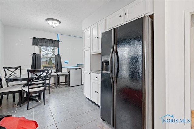 kitchen featuring black refrigerator with ice dispenser, a textured ceiling, light tile patterned floors, fridge, and white cabinets