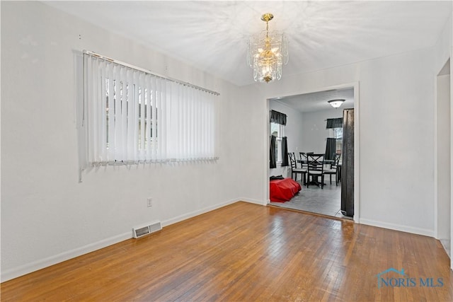 spare room with an inviting chandelier and wood-type flooring