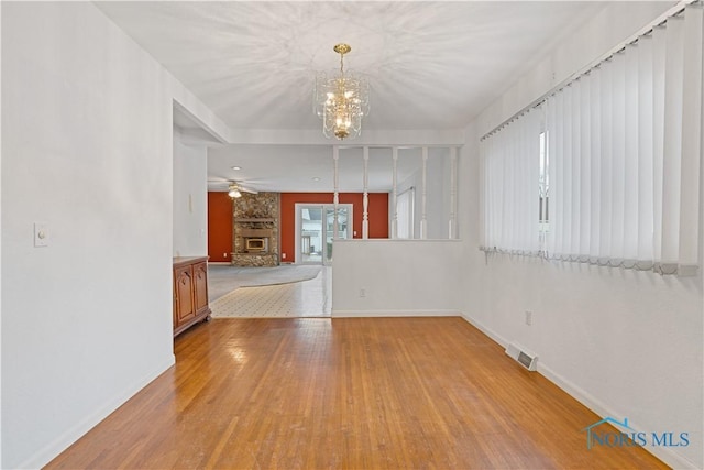 unfurnished room featuring a stone fireplace, ceiling fan with notable chandelier, and light hardwood / wood-style flooring