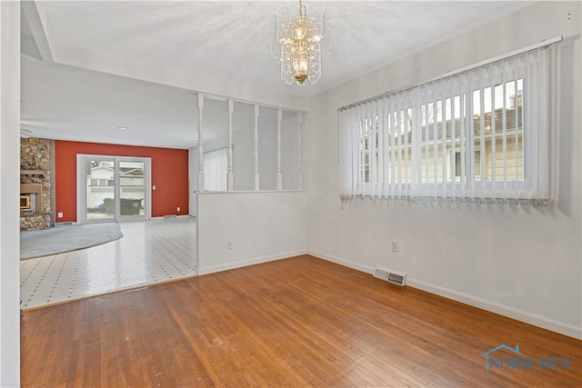 spare room featuring wood-type flooring, a stone fireplace, and a chandelier