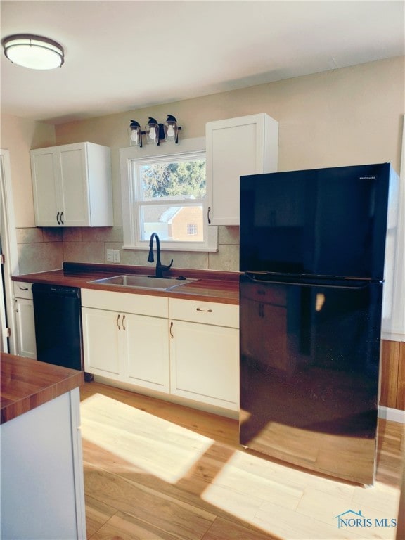 kitchen with butcher block counters, light hardwood / wood-style floors, black appliances, decorative backsplash, and sink