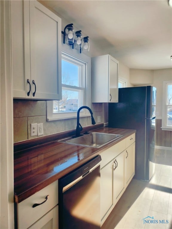 kitchen with white cabinets, dishwasher, wood counters, sink, and tasteful backsplash