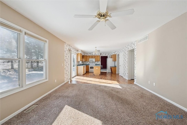 unfurnished living room featuring light colored carpet and ceiling fan with notable chandelier