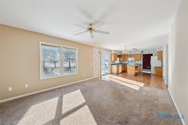 unfurnished living room featuring ceiling fan with notable chandelier and dark carpet