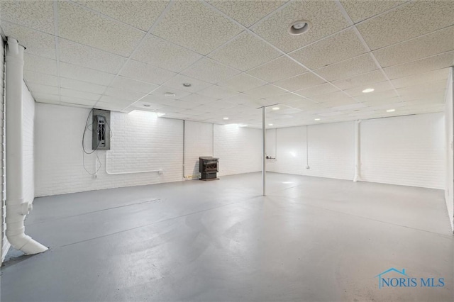 basement with brick wall, a drop ceiling, and a wood stove