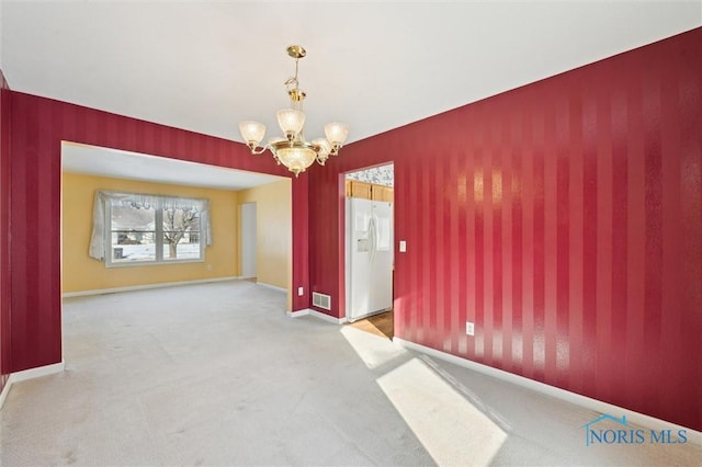 carpeted spare room featuring an inviting chandelier