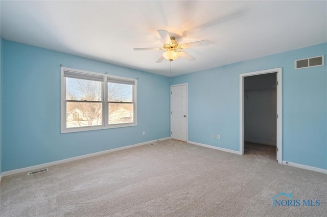 unfurnished bedroom with ceiling fan, a walk in closet, and light colored carpet