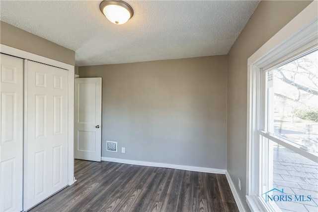 unfurnished bedroom with a textured ceiling, a closet, and dark wood-type flooring