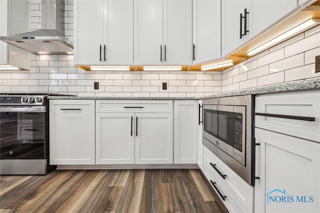 kitchen with decorative backsplash, light stone countertops, wall chimney exhaust hood, stainless steel appliances, and white cabinetry