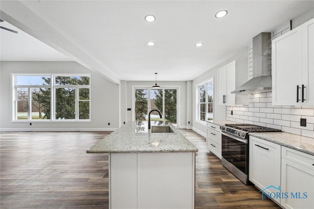 kitchen with white cabinetry, wall chimney range hood, stainless steel range with gas cooktop, an island with sink, and pendant lighting