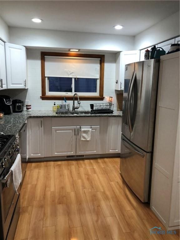 kitchen with dark stone counters, stainless steel appliances, sink, light hardwood / wood-style floors, and white cabinetry