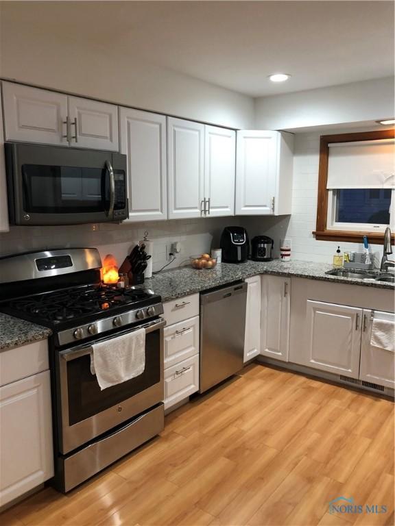 kitchen featuring white cabinets, sink, dark stone countertops, appliances with stainless steel finishes, and light hardwood / wood-style floors