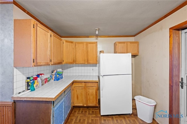 kitchen featuring a textured ceiling, dark parquet flooring, tile counters, white fridge, and ornamental molding