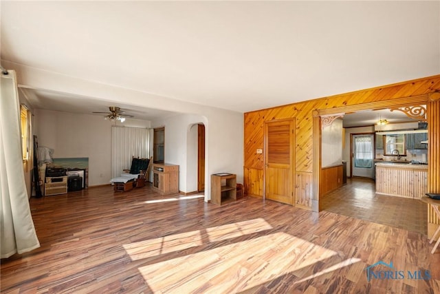 unfurnished living room featuring ceiling fan, wood-type flooring, and wooden walls