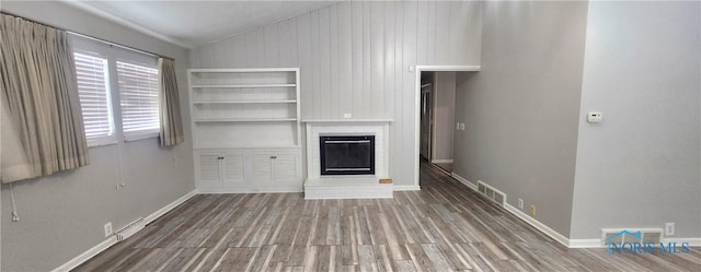 unfurnished living room featuring wood-type flooring, lofted ceiling, a fireplace, and wooden walls