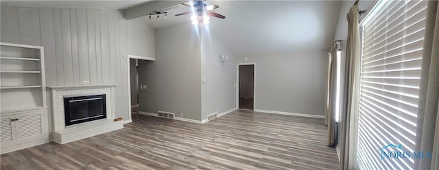 unfurnished living room with built in shelves, ceiling fan, vaulted ceiling with beams, wood walls, and a fireplace